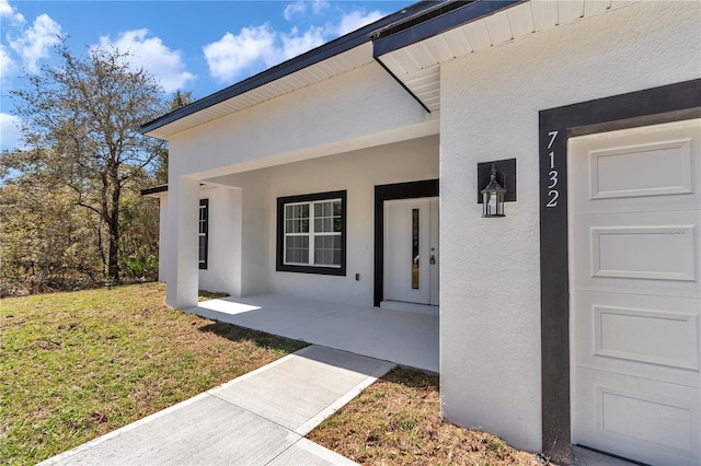 view of exterior entry with covered porch, stucco siding, and a yard