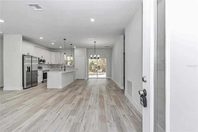 kitchen with visible vents, stainless steel appliances, light countertops, a notable chandelier, and open floor plan