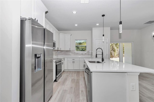 kitchen featuring visible vents, a center island with sink, a sink, stainless steel appliances, and light countertops