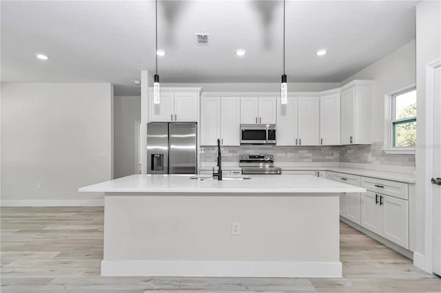 kitchen featuring visible vents, a center island with sink, a sink, backsplash, and stainless steel appliances