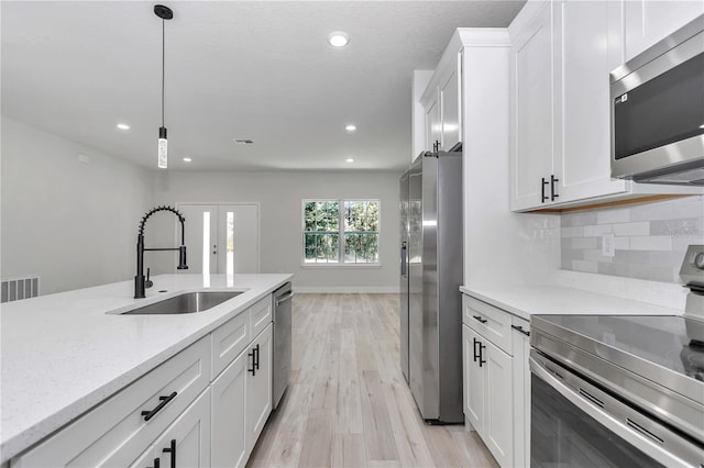 kitchen featuring a sink, light wood-style floors, appliances with stainless steel finishes, decorative light fixtures, and tasteful backsplash