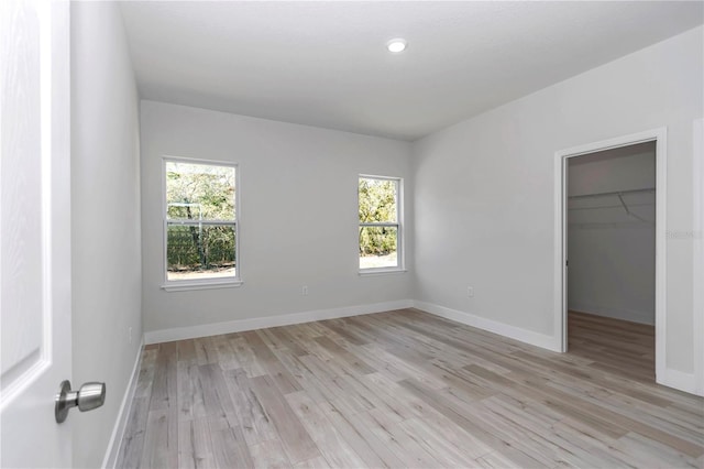 unfurnished bedroom with a closet, baseboards, light wood-style flooring, and a spacious closet