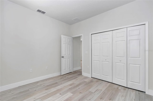 unfurnished bedroom featuring light wood-style flooring, baseboards, visible vents, and a closet