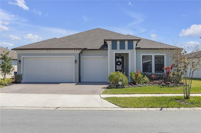 prairie-style house with stucco siding, decorative driveway, a garage, and a shingled roof