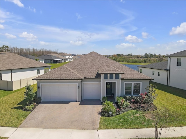 ranch-style home featuring decorative driveway, a garage, roof with shingles, and a front lawn