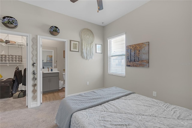 bedroom with light carpet, a ceiling fan, ensuite bathroom, a closet, and a spacious closet