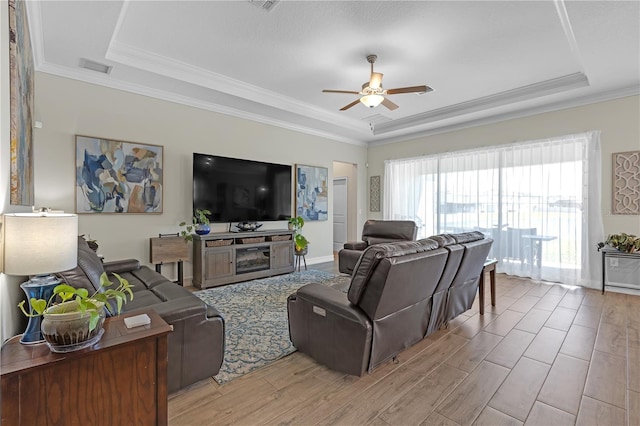 living room featuring a tray ceiling, crown molding, a ceiling fan, and light wood finished floors