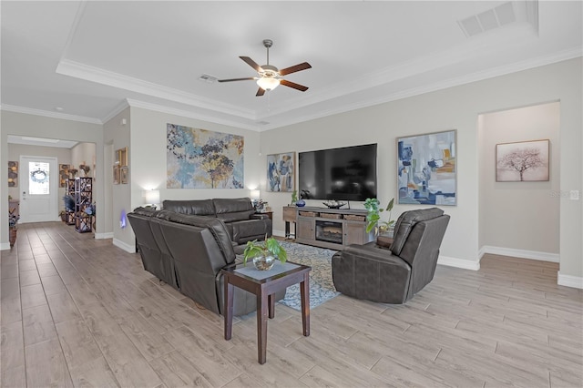 living room with light wood-type flooring, a raised ceiling, visible vents, and a ceiling fan