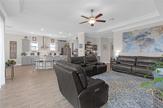 living area with a ceiling fan, visible vents, a tray ceiling, light wood-style floors, and crown molding