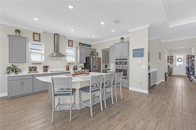 kitchen with visible vents, gray cabinets, a sink, stainless steel appliances, and wall chimney range hood