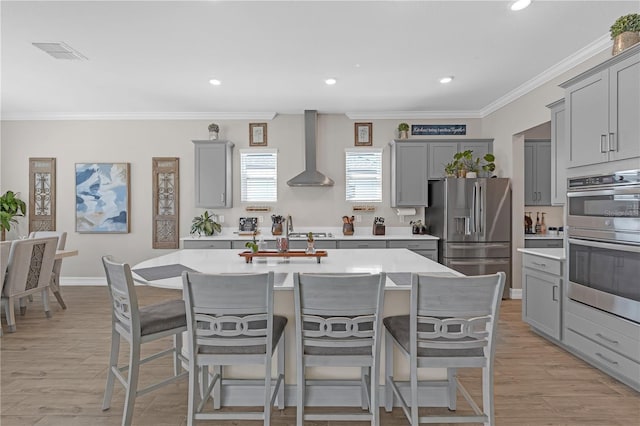 kitchen with wall chimney range hood, visible vents, stainless steel appliances, and gray cabinetry