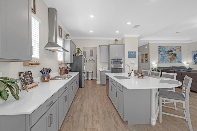 kitchen with visible vents, wall chimney range hood, gray cabinets, appliances with stainless steel finishes, and a kitchen breakfast bar