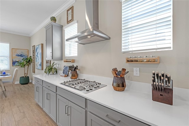 kitchen with gray cabinetry, wall chimney range hood, stainless steel gas cooktop, light countertops, and ornamental molding