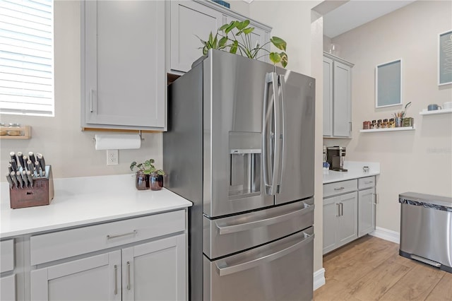 kitchen with open shelves, light wood-style flooring, gray cabinetry, light countertops, and stainless steel refrigerator with ice dispenser