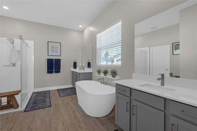 bathroom with a shower stall, a freestanding bath, two vanities, wood finished floors, and a sink