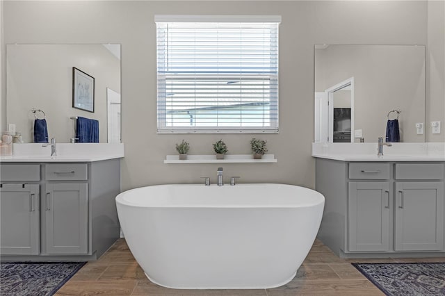 bathroom with wood tiled floor, a freestanding tub, two vanities, and a sink