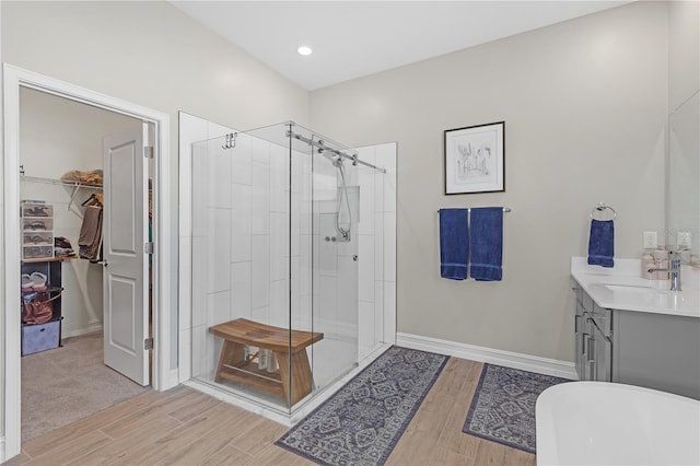 full bathroom with vanity, wood finished floors, a soaking tub, a shower stall, and a walk in closet