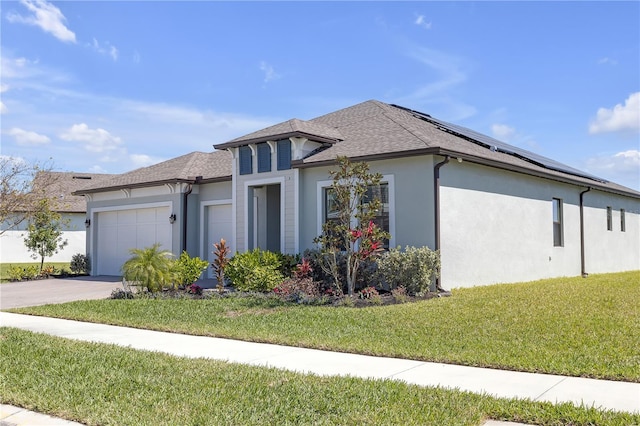 prairie-style home with stucco siding, a front lawn, roof mounted solar panels, an attached garage, and a shingled roof