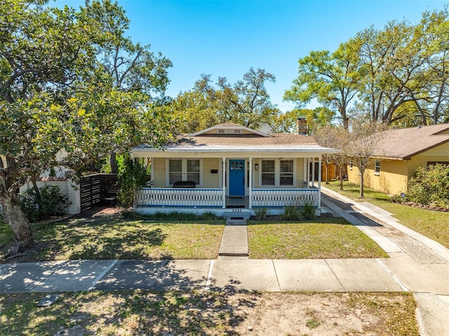 bungalow-style home featuring a chimney, a porch, and a front lawn