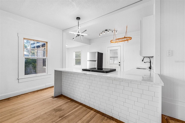 kitchen featuring a peninsula, freestanding refrigerator, a sink, a textured ceiling, and light wood-type flooring