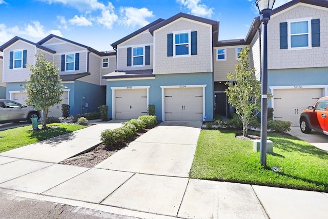 multi unit property featuring a garage, concrete driveway, a front lawn, and stucco siding