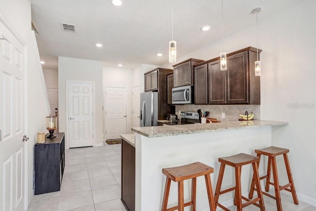 kitchen featuring stainless steel appliances, a kitchen bar, backsplash, and dark brown cabinets