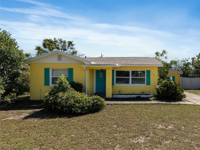 view of front facade featuring stucco siding, a front lawn, and fence