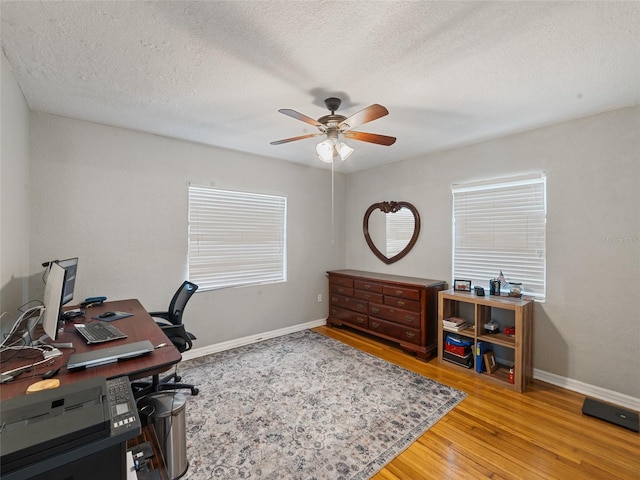 office area with light wood-style flooring, a textured ceiling, baseboards, and a ceiling fan