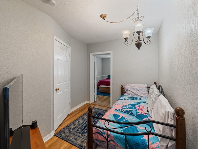 bedroom with baseboards, a notable chandelier, wood finished floors, and a textured wall