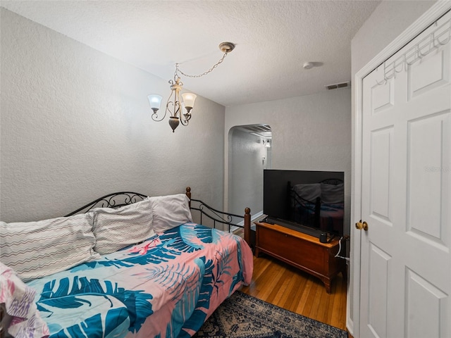 bedroom with wood finished floors, visible vents, a textured ceiling, a textured wall, and a chandelier