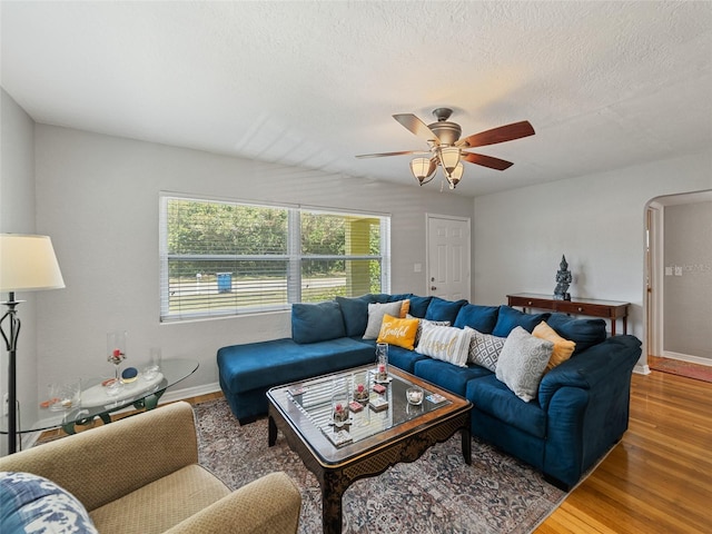 living room featuring arched walkways, a textured ceiling, baseboards, and wood finished floors