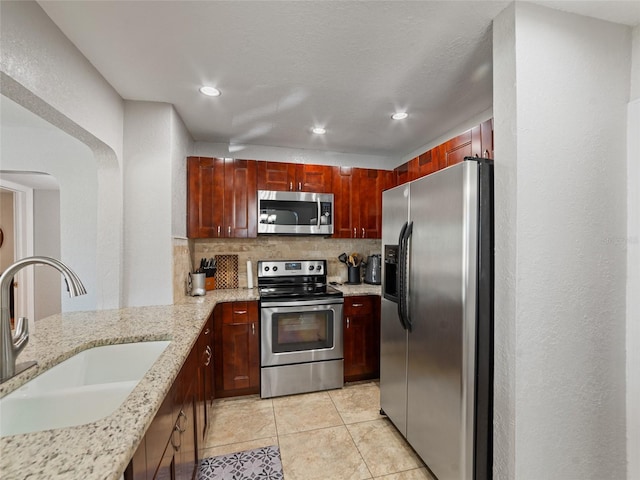 kitchen featuring a sink, light stone counters, backsplash, recessed lighting, and appliances with stainless steel finishes