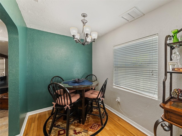 dining space with arched walkways, visible vents, baseboards, and wood finished floors