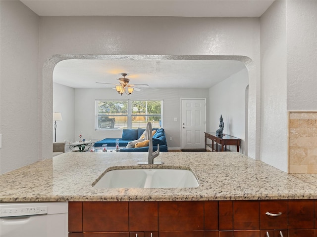 kitchen featuring light stone countertops, a sink, dishwasher, a textured wall, and open floor plan