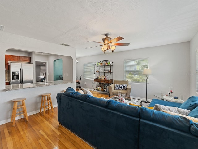 living area featuring ceiling fan, visible vents, arched walkways, and light wood-style flooring