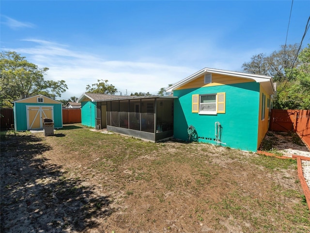 rear view of property featuring a lawn, a storage shed, a fenced backyard, a sunroom, and an outbuilding