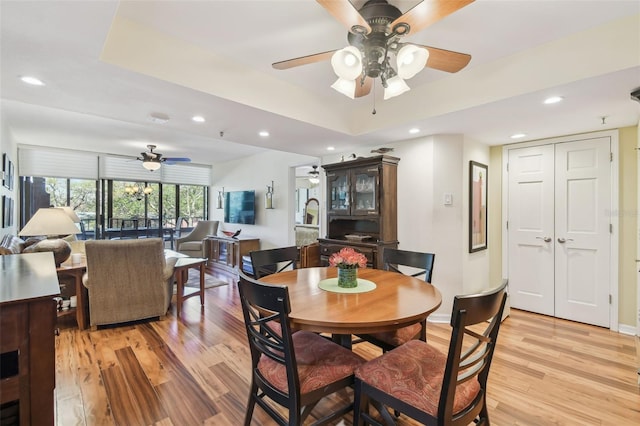 dining area featuring recessed lighting, light wood-style flooring, a raised ceiling, and a ceiling fan