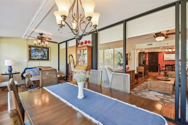 dining space with ceiling fan with notable chandelier, a textured ceiling, a textured wall, and wood finished floors