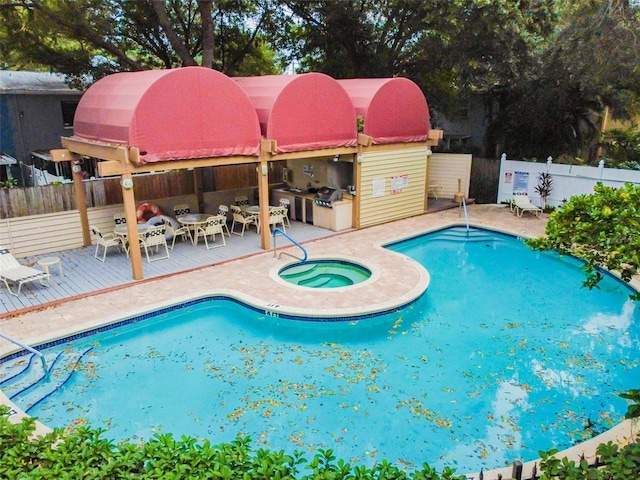 community pool featuring fence, a wooden deck, exterior kitchen, outdoor dining space, and a community hot tub