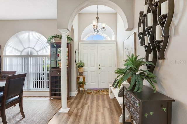 entrance foyer with an inviting chandelier, decorative columns, wood finished floors, and a healthy amount of sunlight