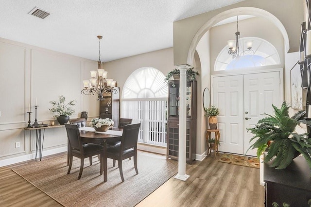 dining space with light wood-type flooring, visible vents, a notable chandelier, and decorative columns