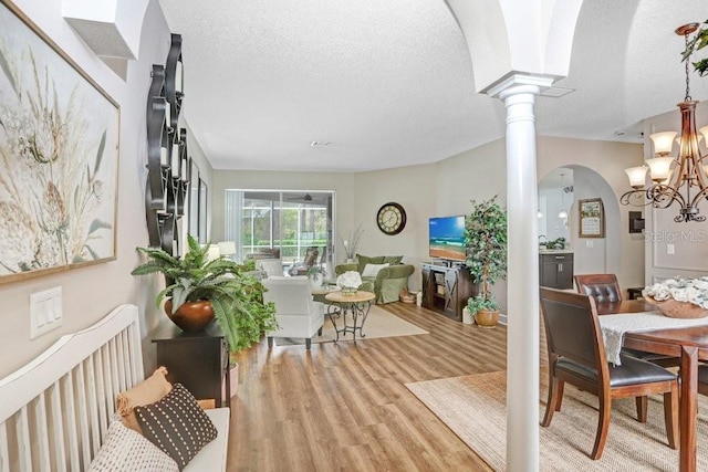 dining space featuring light wood-style flooring, decorative columns, arched walkways, a textured ceiling, and a notable chandelier