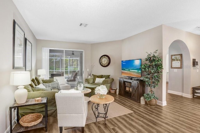 living area featuring visible vents, baseboards, wood finished floors, arched walkways, and a textured ceiling