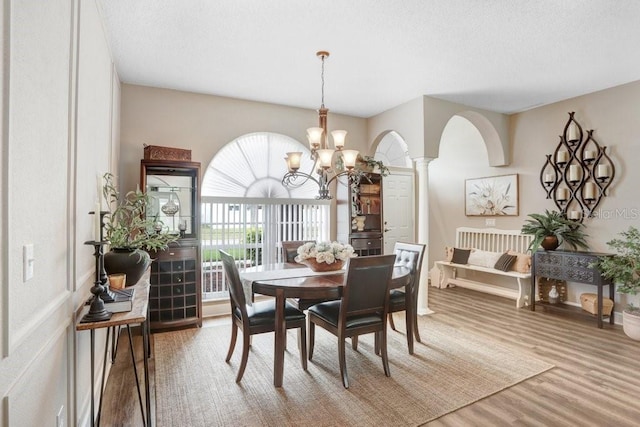 dining room featuring wood finished floors, ornate columns, arched walkways, a textured ceiling, and a chandelier