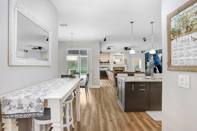 kitchen featuring visible vents, ceiling fan, a fireplace, and light wood finished floors