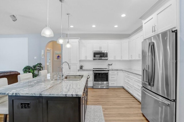 kitchen with arched walkways, appliances with stainless steel finishes, white cabinetry, and a sink