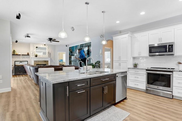 kitchen featuring ceiling fan, a fireplace, white cabinets, stainless steel appliances, and a sink