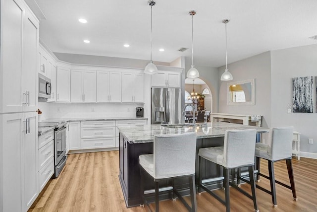 kitchen featuring an island with sink, stainless steel appliances, white cabinets, a kitchen breakfast bar, and light wood-type flooring