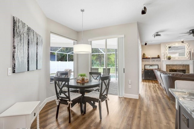 dining room featuring a fireplace, baseboards, a ceiling fan, and wood finished floors