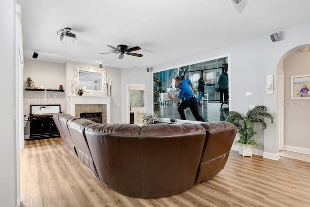 living room with baseboards, light wood-style floors, arched walkways, a glass covered fireplace, and a ceiling fan